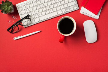 Top view photo of white keyboard mouse flowerpot glasses clips pen red cup of coffee and two...