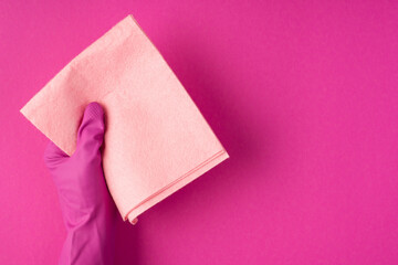 Top view photo of hand in pink glove holding pastel pink napkin on isolated pink background with copyspace