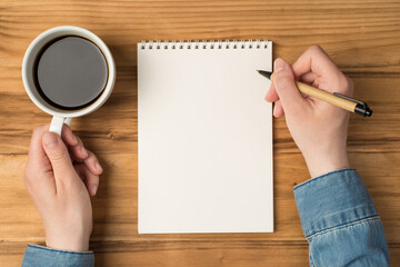 Overhead photo of notebook paper hands with pen and cup of coffee isolated on the wooden backdrop