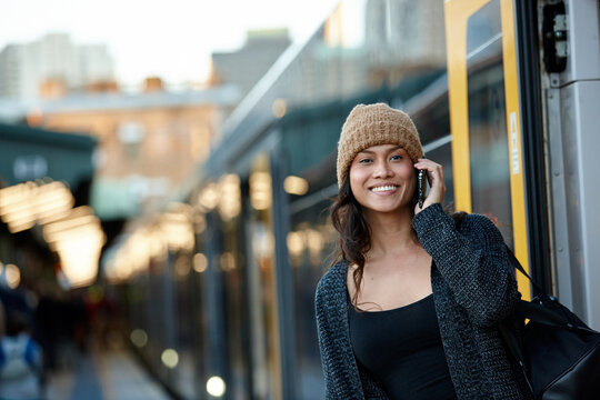 Happy Asian woman getting off train talking on mobile phone