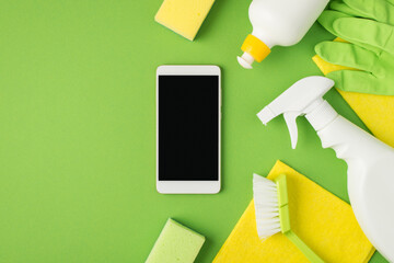 Top view photo of smartphone display in the middle detergent spray and gel bottles scouring pads brush yellow napkins green rubber gloves on isolated green background with copyspace