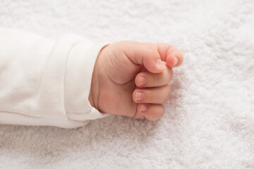 Closeup photo of newborn baby's tiny hand on isolated white textile background