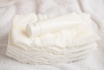 Closeup photo of white cream tube without label on diapers on isolated white textile background