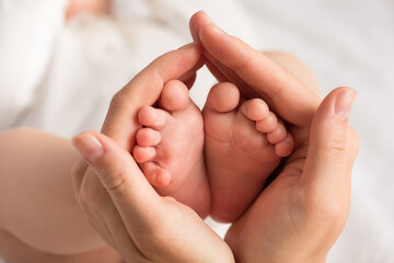 Obraz na płótnie Canvas Closeup photo of newborn's feet in mother's palms on isolated white textile background