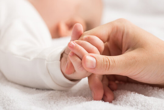 Closeup photo of newborn's small hand clenching mother's forefinger on isolated white textile background