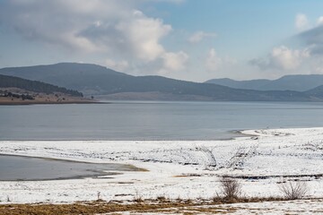 Natural landscape. Beautiful white snow on the coast and frozen water surface of Batak Dam, lake in the Rhodope Mountains, Bulgaria. Fog over the distant coast.