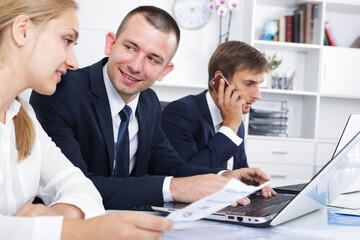 Fototapeta premium Laughing business male and female assistants in formalwear working on laptops and talking on mobile phone in firm office