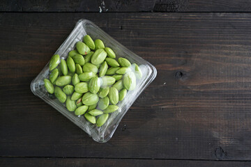 Bitter bean, twisted cluster bean, or stink bean wrapped in plastic on a black wooden table. In Indonesia its called 