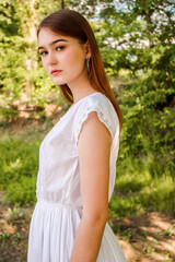 Portrait of a perfect girl in a park or in nature. Beautiful shape of body. Lovely girl's face. Green background. Expressive look. Girl's glance. White beautiful model