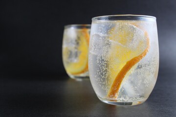 lemonade with orange and ice in a glass on a black background next to lies ice and orange. Summer drink on a black background