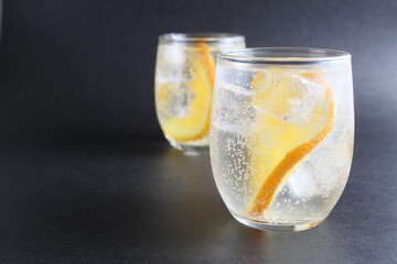 lemonade with orange and ice in a glass on a black background next to lies ice and orange. Summer drink on a black background