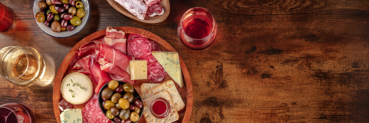 Charcuterie and cheese board panorama with red wine and olives, shot from the top on a rustic...