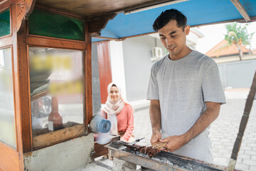 man street food seller of chicken satay with food cart selling sate ayam. proud of small business owner doing his job