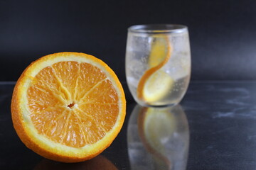 lemonade with orange and ice in a glass on a black background next to lies ice and orange. Summer drink on a black background