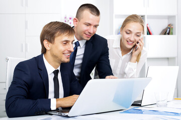 Three smiling business colleagues working and discussing working task on phone in office. Focus on the left man