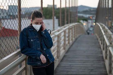 Young girl with ffp2 mask talking on the phone on the bridge