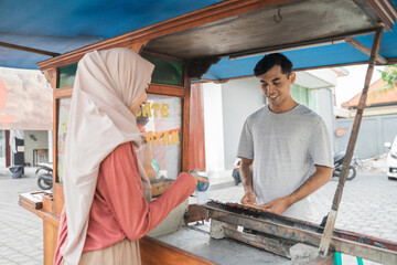 muslim woman ordering chicken satay from small food cart seller. sate ayam street food