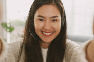 Young Attractive Smiley Asian woman wearing headset doing video chat in the living room. Asian instructor wearing headphone getting ready for online class at home.
