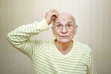 Senior man in eyeglasses touches head with hand and thinks of something.