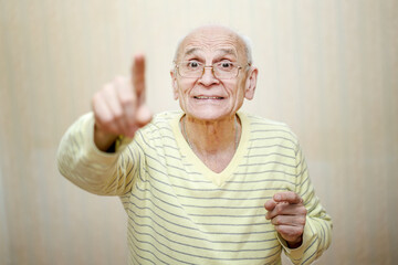Aged old man wearing eyewear pointing finger up and smiling.