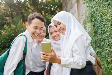 four teenagers in junior high school uniforms using and looking at cellphones on the school grounds