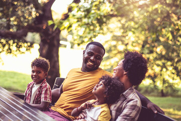 African American family sitting on bench in park.