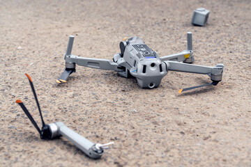 the fall of the drone. a broken flying quadcopter is lying on the asphalt, the propeller has flown off and the camera is damaged