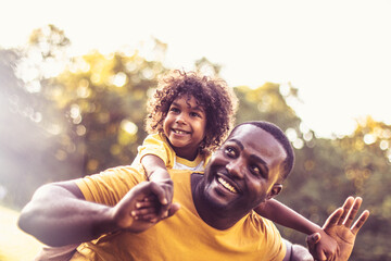 Father carrying daughter piggyback. African American father and daughter having fun outdoors.