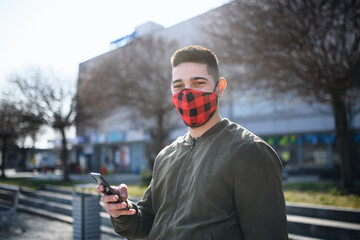 Young man outdoors on street in town using smartphone, coronavirus and new normal concept.