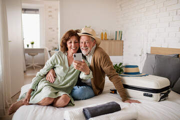 Happy senior couple with smartphone in hotel room, taking selfie.