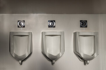 Closeup of three white seperated urinals and automatic infrared flushing in men\'s bathroom, design...
