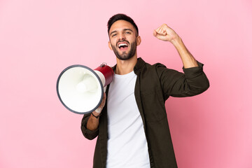 Young caucasian man isolated on pink background shouting through a megaphone to announce something