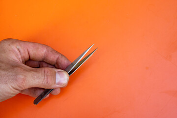 Male hand with tweezers in front of orange background. Copy Space on the right side.