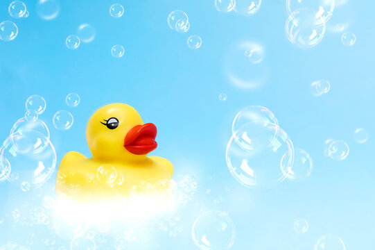 Yellow rubber duck on light blue background with soap bubbles. Banner image