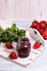 Jar of strawberry jam on wooden rustic board. Sweet berry dessert on a kitchen table. Copy space for your text