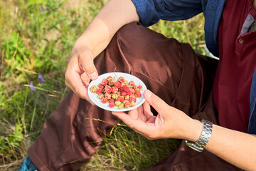 A white saucer with a wild berry in men's hands in a forest clearing.