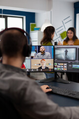 Videographer employee having video conference wearing headset editing client movie, getting...