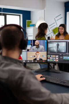 Videographer employee having video conference wearing headset editing client movie, getting feedback on commercial project. Freelancer using post production software on pc in creative office.