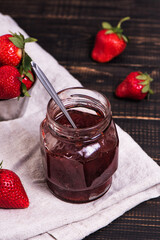 Jar of strawberry jam on wooden rustic board. Sweet berry dessert on a kitchen table. Copy space for your text