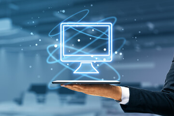 Hand holding glowing computer monitor icon hologram on blurry office interior background. Smart technology and innovation concept.