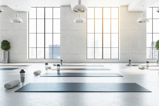 Stylish bright white yoga studio gym interior with brick wall, window and city view. 3D Rendering.