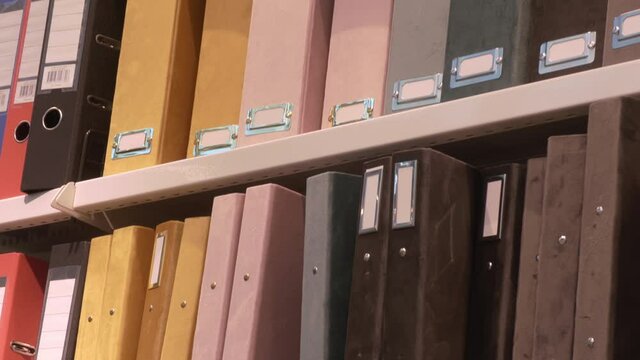 Closeup shot of different colors of storage folders for documents in shelves. Camera slowly tilting downwards.