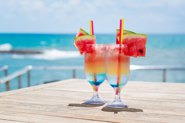 Two rainbow cocktails on a wooden table at seashore. Concept of luxury vacation. Colorfull...