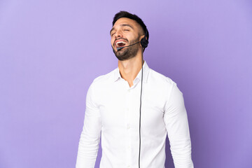 Telemarketer man working with a headset isolated on purple background laughing