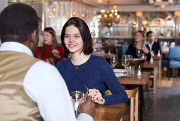 Young woman with African American colleague on friendly meeting over dinner with wine in restaurant