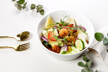 Appetizing summer salad with fresh vegetables, fried shrimps, cheese and herbs. Seasonal vegetables, seafood and goat cheese. Healthy Mediterranean food and diet. Cutlery. White background.