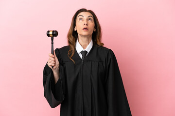 Middle aged judge woman isolated on pink background looking up and with surprised expression