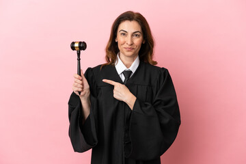 Middle aged judge woman isolated on pink background pointing to the side to present a product
