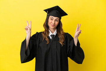 Middle aged university graduate isolated on yellow background showing victory sign with both hands