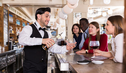 Handsome hispanic barman serving drinks to young people on bar in restaurant